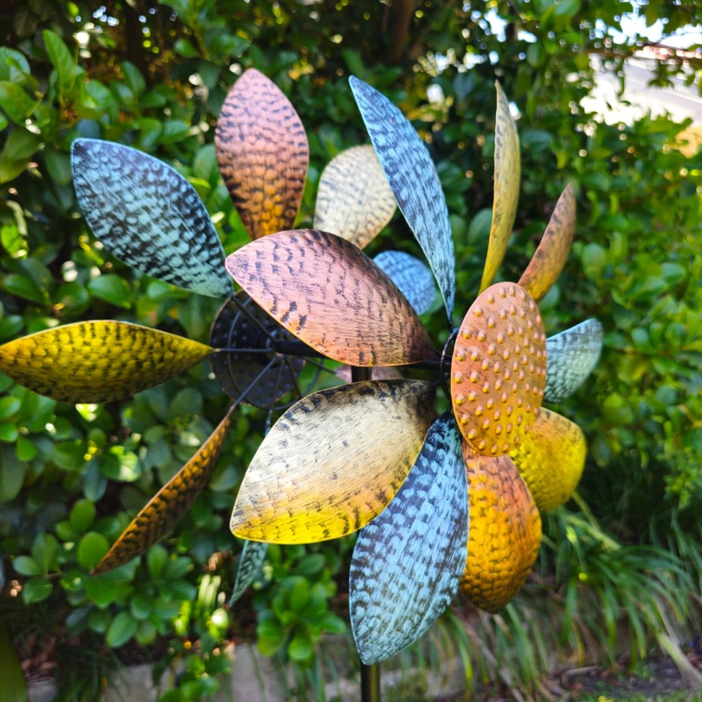Daisy design wind spinner with bronze, gold and blue textured petals spinning in garden
